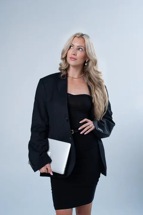 Olivia Malcher in schwarzem Blazer trägt einen Laptop im Arm