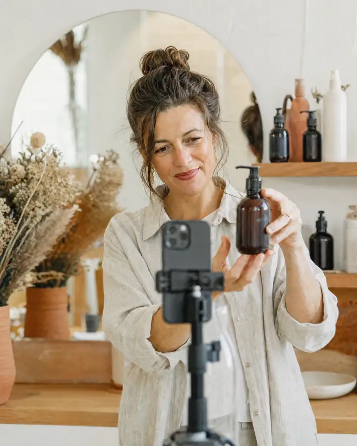 Symbolbild: Frau hält eine Pumpflasche vor ein Smartphone auf dem Stativ und dreht ein Produktvideo