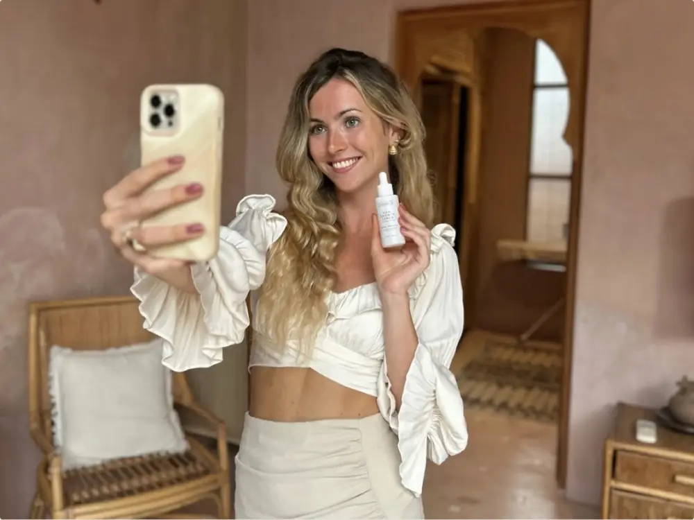 Symbolbild: Frau filmt mit dem Smartphone ein Selfie-Video und hält dabei ein Pflegeprodukt