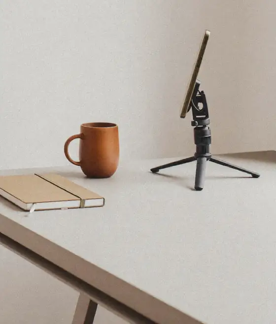 Symbolbild: Smartphone-Stativ neben Tasse und Notizbuch auf einem Tisch