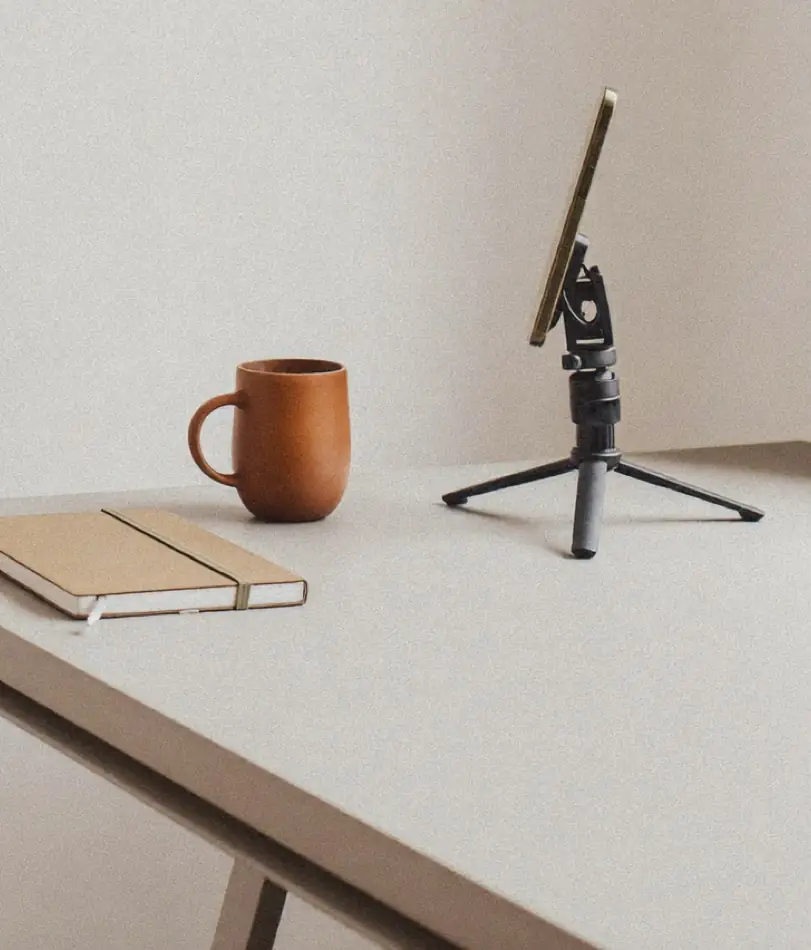 Symbolbild: Smartphone-Stativ neben Tasse und Notizbuch auf einem Tisch