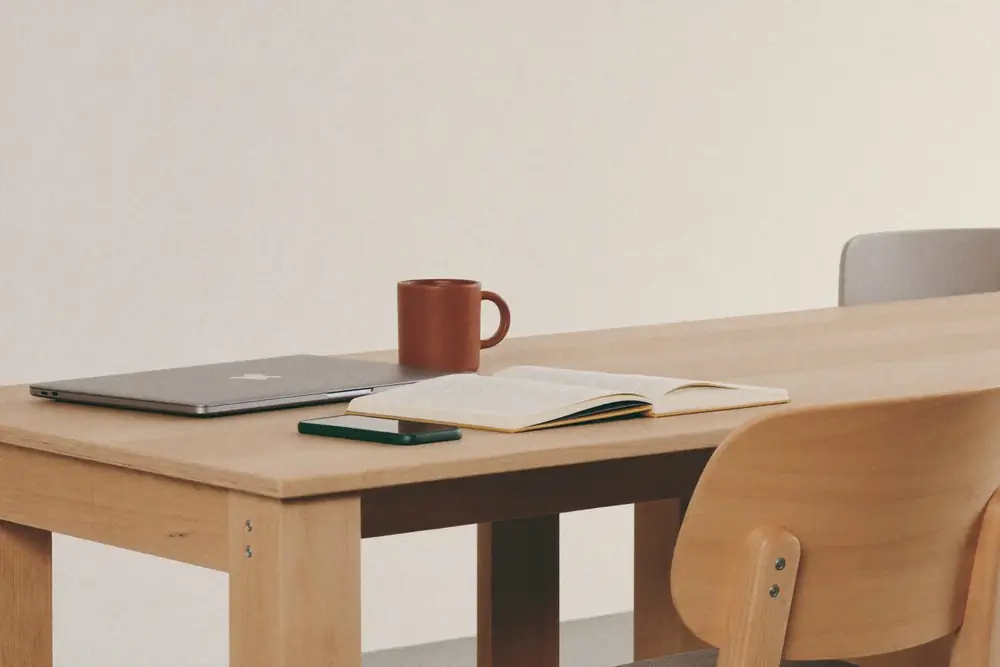Symbolbild: Holztisch mit Laptop, Notizbuch und Tasse – ein ruhiger Arbeitsplatz